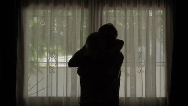 silhouette woman and man hug each other whole heartedly against room window