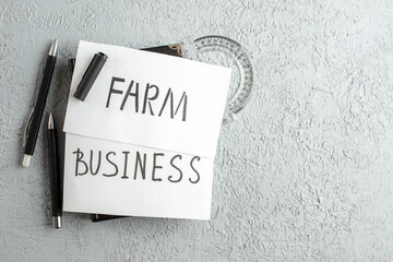 Top view of BUSINESS and FARM writings on white sheets ruler pens on the right side on gray sand background with free space