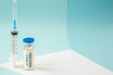 Top view of covid- vaccine in medical ampoule and empty disposable syringe on the right side on blue background