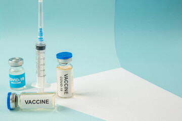 Top view of covid- vaccine in medical ampoules and empty disposable syringe on a white blank on blue background