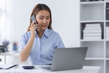 Cheerful business Asian woman freelancer making telephone call share good news about project working in office workplace, business finance concept.	