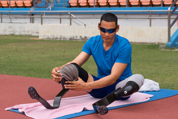 portrait of an Asian paralympic athlete, seated on a stadium track, busily affixing his running...