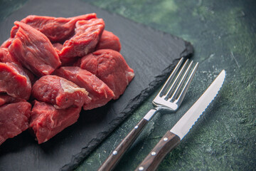 Top view of fresh chopped raw meat on wooden board and cutlery set on the right side on green black mix colors background
