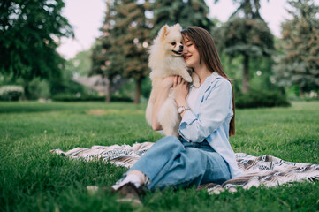 Young woman with her cute dog in park. Pomeranian Spitz with his owner are sitting on the grass.