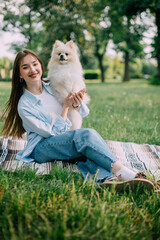 Young woman with her cute dog in park. Pomeranian Spitz with his owner are sitting on the grass.