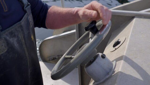 Close up of a male sailor stearing the helm of a boat wearing overalls