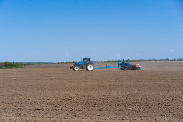 Obraz premium The tractor drives across the field and cultivates the land. Agricultural vehicle works in countryside. Sowing is the process of planting seeds in the ground as part of the early spring time