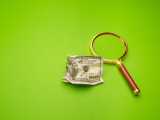 Financial crisis in the USA. One hundred US dollar banknote crumpled and a magnifier on a green background