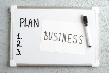 Top view of PLAN and numbers on white desk BUSINESS writing marker on white sheet on gray sand background