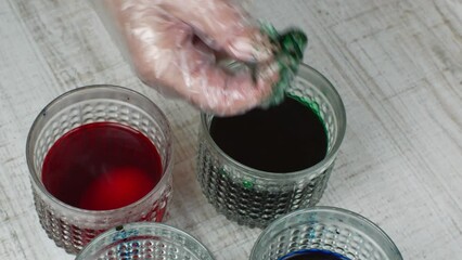 A housewife paints a white chicken egg green. Close-up of a female hand laying a white chicken egg in a glass with green paint. The concept of painting white chicken eggs for the Easter holiday