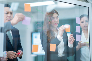 executives business asian entrepreneur of small company putting a adhesive note on glass in office during team meeting formulating business strategies.