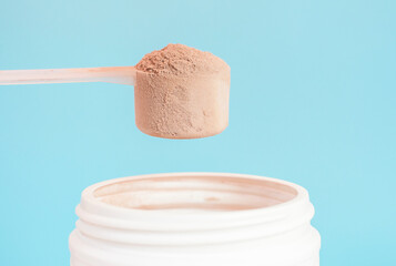 Chocolate protein powder in scoop and plastic jar on blue background. - obrazy, fototapety, plakaty