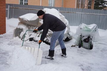 A man cleans snow in the winter in the courtyard of the house.