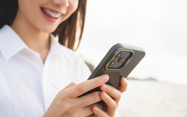 Woman traveling standing on the beach with hand holding smartphone with using social media on internet. Summer lifestyle.