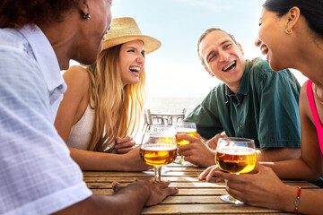 Group of multiracial young friends laughing having fun at beach bar drinking beers together....
