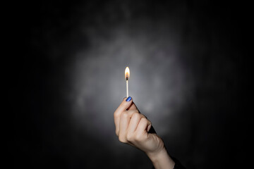 Woman's hand holding lit match on black background.