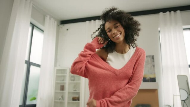 Girl dancer dancing at home. Black young girl with pretty curly hair moves in rhythm. Pretty biracial dancer woman happy smiling satisfied facial expressions. Beautiful biracial diverse model freedom