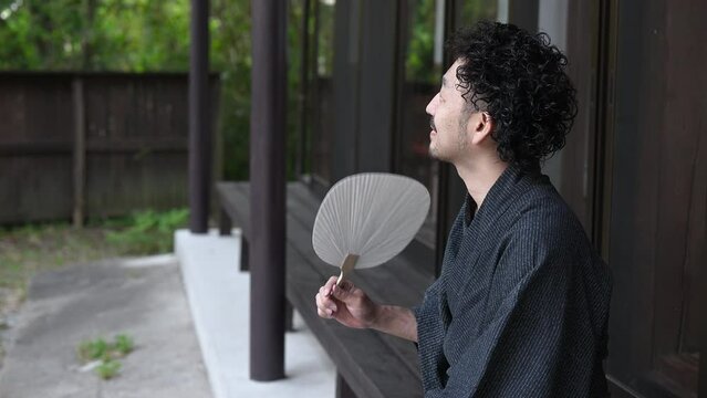 うちわをもって縁側でくつろぐ浴衣の日本人男性 夏の旅館や旅行のイメージの動画