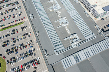 shingle roof of shopping mall with ventilation system. parking lot with parked cars. aerial top view.