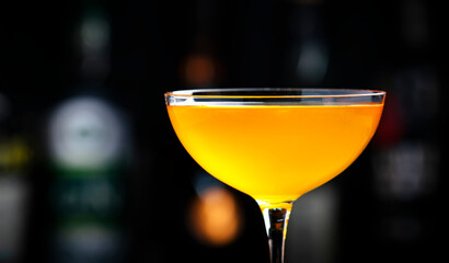 Golden alcoholic cocktail drink with whiskey, apple liqueur, ginger syrup, lemon juice, green basil and ice, dark bar counter background, close-up
