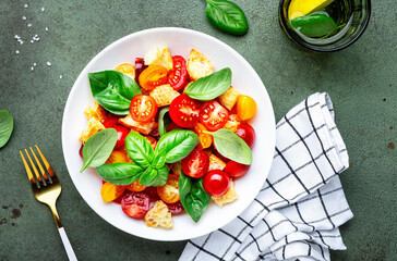 Panzanella summer vegetable salad with stale bread, colorful tomatoes, olive oil, salt and green basil, green table background, top view