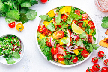 Gourmet salad with grilled chicken and mango salsa, tomato, cilantro, onion and lettuce in mexican style, white kitchen table background, top view