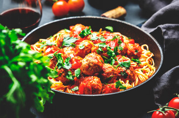 Prepared spaghetti pasta with fried pork meatballs in tomato sauce with parsley in frying pan, black table background, top view