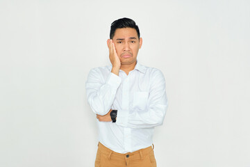 Portrait of bored young Asian man in casual clothes holding his cheek and feeling frustrated, having problems isolated on white background