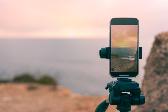  beautiful seascape has a place for an inscription close-up on the phone,smartphone camera stands on a tripod close-up, photographing a picturesque evening sunset over a tropical sea and a mountain.
