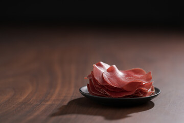 saucer with this slices of bresaola on walnut wood table
