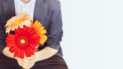 Background with a schoolboy with a bouquet of colorful gerbera flowers in his hands. Concept of the end or beginning of the school year and back to school. First high school love. Copy space