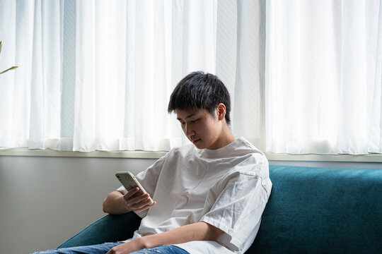 ソファーに座りスマートフォンを見る若い日本人男性