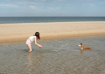 Beautiful fashionable young girl having fun on the beach barefoot with her dog