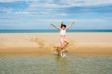 Fototapeta na wymiar Beautiful fashionable young girl having fun on the beach barefoot with her dog