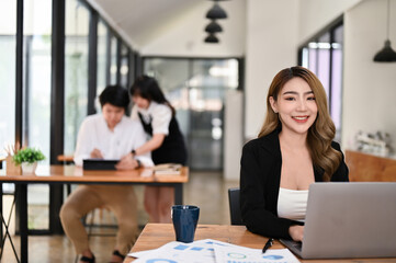 A businesswoman is smiling at the camera while sitting at her desk in the office.