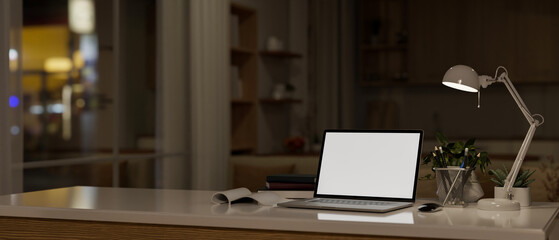 A laptop white screen mockup on a table in a modern dark living room at night.
