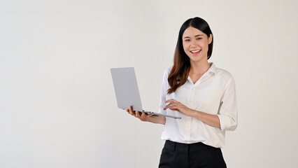 A businesswoman stands against a white studio background with her portable laptop.