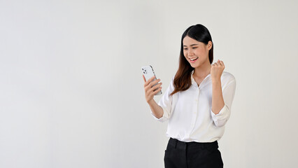 A cheerful Asian female is showing her fist while looking at her smartphone screen