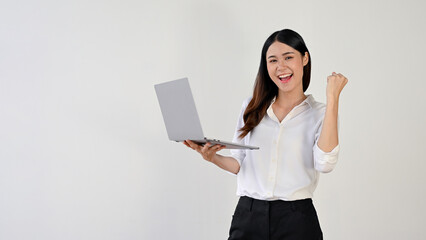 A cheerful Asian woman shows her fist while holding her laptop. success, celebrating