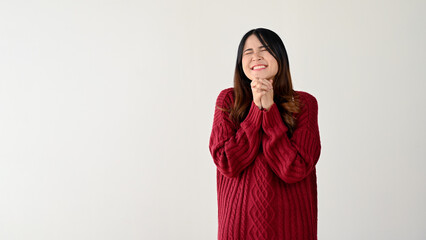 Fototapeta premium A lovely Asian woman is holding clasped hands over her chest, smiling, and closing her eyes