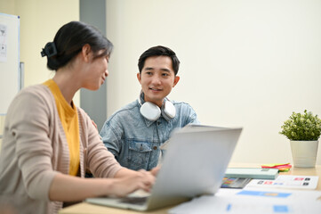 Obraz premium A smart Asian male UX graphic designer is discussing work with his female colleague in the office