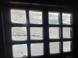 Cabin window on top of the mountain with snow and sky view