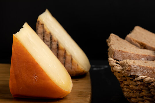Mah&oacute;n Menorca cheese. Semi-cured and cured cheese wedges on a wooden board next to a basket of brown bread. Food from the Balearic Islands (Spain).