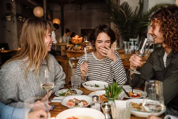 Gordijnen Group of friends drinking wine while dining in restaurant © Drobot Dean
