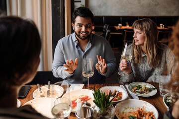 Group of young friends talking while dining in restaurant
