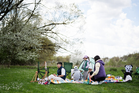 Happy young family, mother and four children having fun and enjoying outdoor on picnic blanket painting at garden spring park, relaxation.