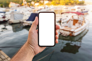 Man holding mockup smartphone with blank white touch screen at sea water's edge