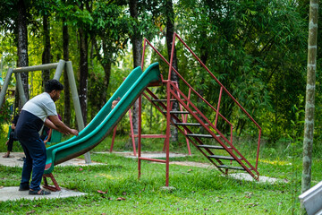 South asian young father playing in park slide with his little son , happy family moments 