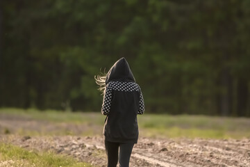 Dziewczyna w kapturze z rozwianymi włosami spaceruje między polami