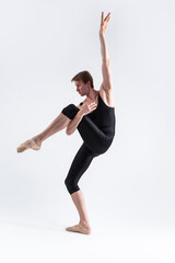 Male Ballet Dancer Man in Black Dance Suit Tights Posing in Ballanced Dance Pose While Stretching His Arm and Leg Muscles in Studio on White.